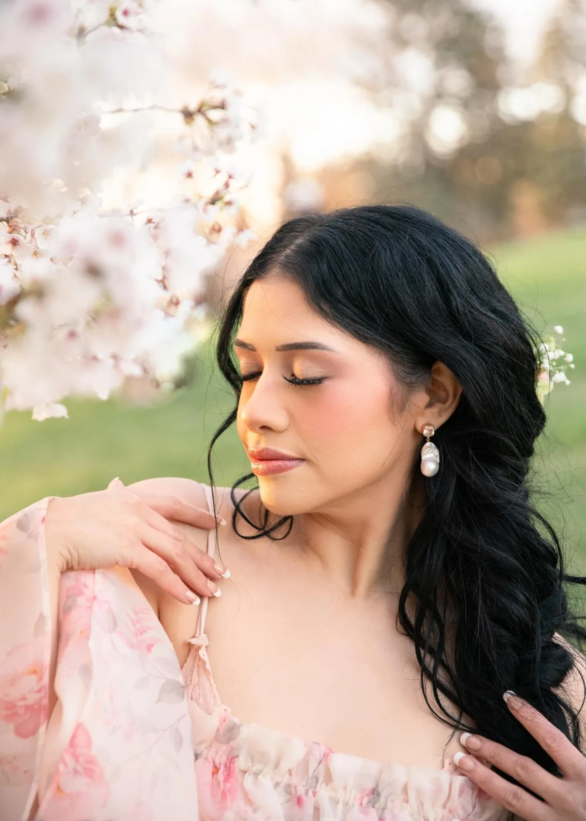 Bride with dark curled hair and rosy glam makeup among spring blossoms