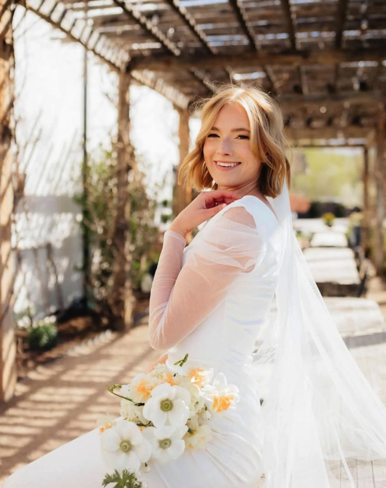 Bride with a romantic updo and long veil under a garden pergola