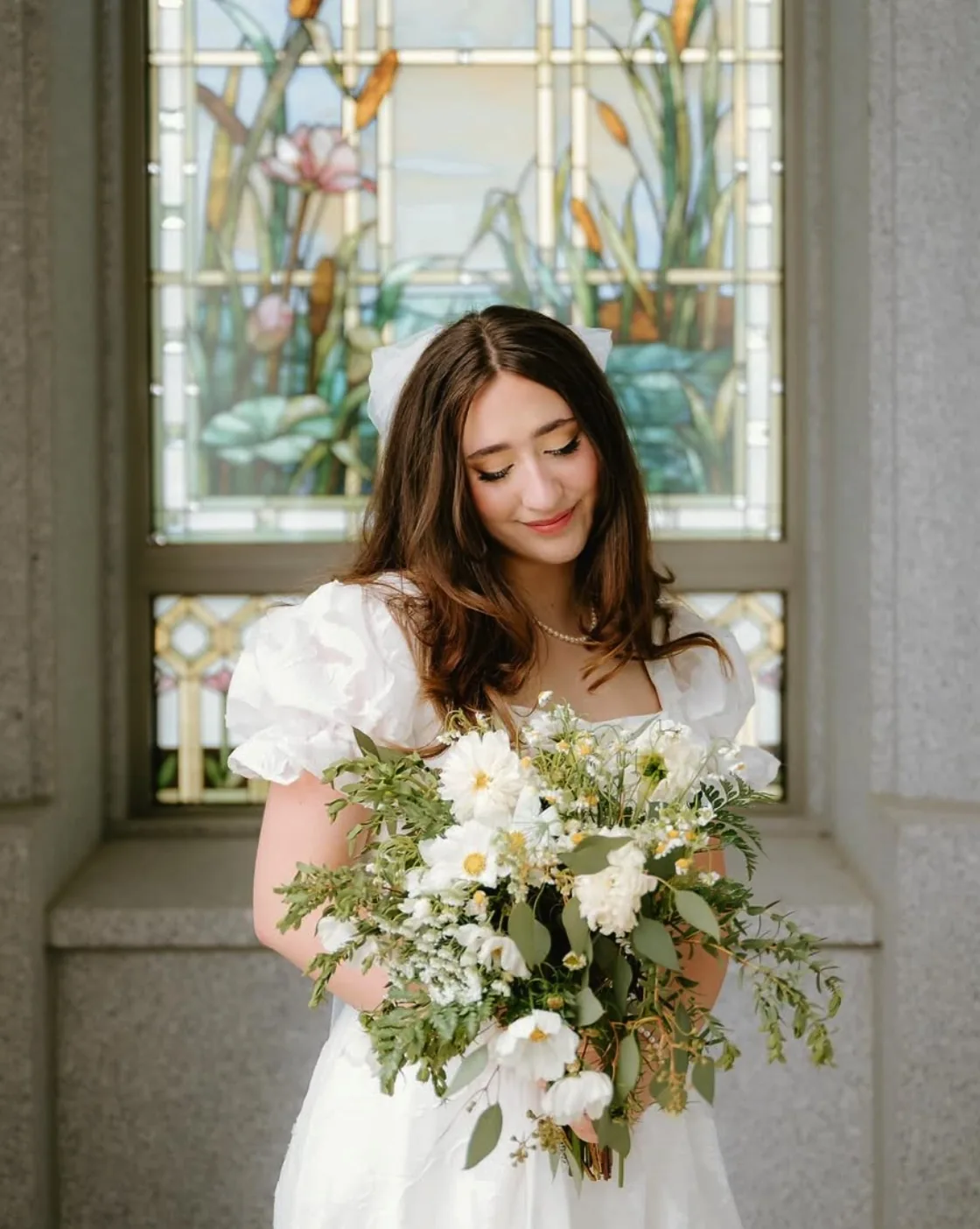 Bride with soft curls and natural makeup by a stained-glass window