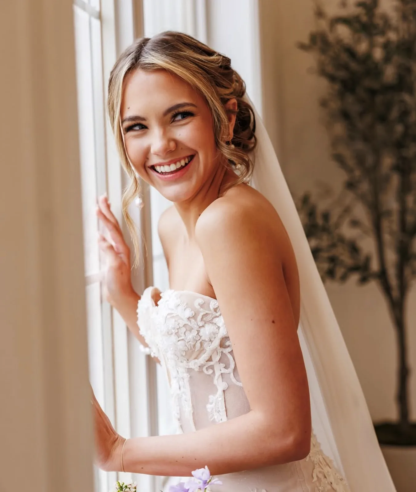 Smiling bride with an elegant updo and veil by a sunlit window