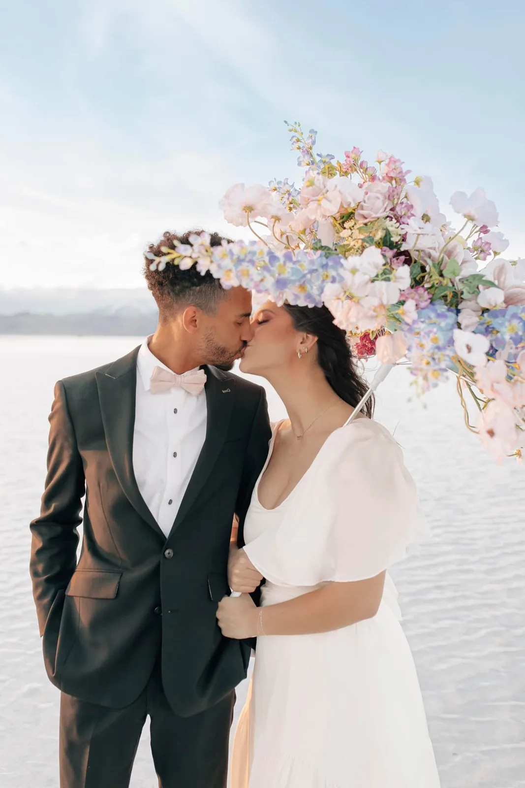 Bride and groom kissing under a floral parasol on the salt flats