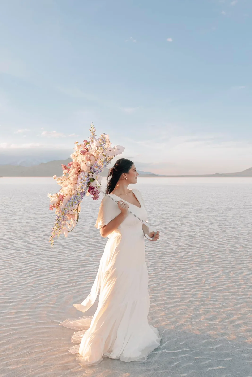 Bride carrying a floral parasol across the reflective Utah salt flats
